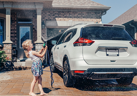 child playing with water hose washing car